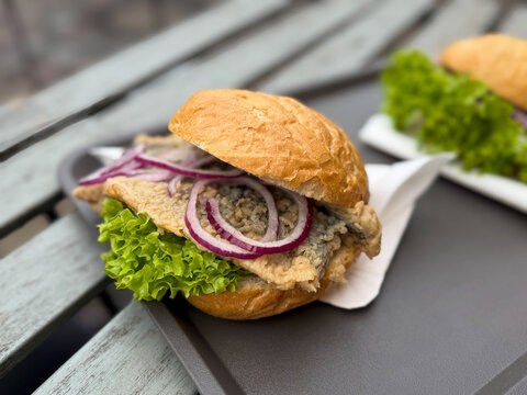 Traditional north germany snack street food Fischbroetchen fish sanwich with fried herring, matjes, onion and salad leaves in a wheat bun on a table close up on Fischmarkt in Hamburg