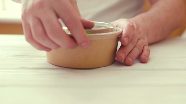 Closeup of man paking up a fresh healthy salad to a zero waste container to go. Food delivery, healthy food concept.