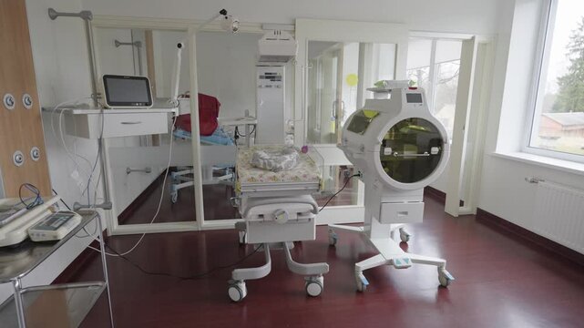  Bright neonatal hospital room with advanced incubators, a baby bed, monitors, and medical devices for infant care, all on wheeled units.