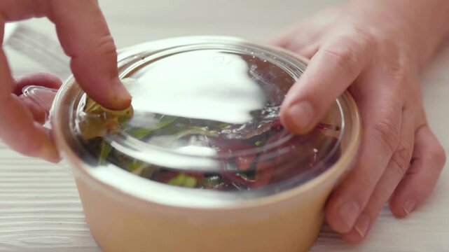 Closeup of man paking up a fresh healthy salad to a zero waste container to go. Food delivery, healthy food concept.