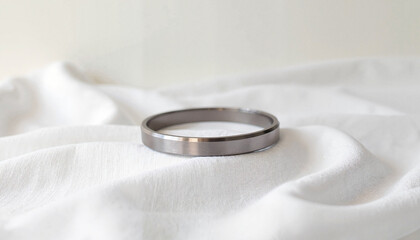Sleek silver ring resting on soft white fabric background  