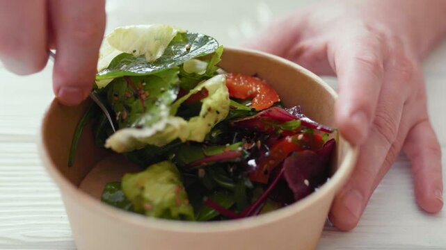 Closeup of man eating a fresh healthy salad from a zero waste container to go. Food delivery, healthy food concept.