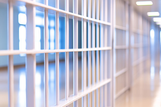 Close-up of metal prison bars in brightly lit corridor with modern architecture and reflections on polished floor