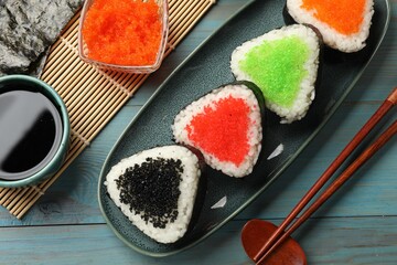 Tasty tobiko onigiri (Japanese rice balls) served on light blue wooden table, flat lay