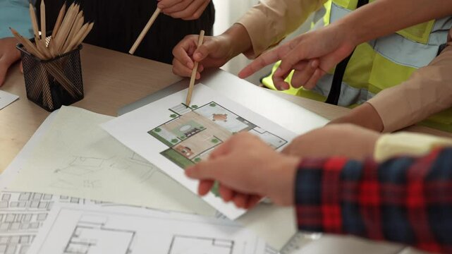Smart architect and safety engineer discussion about building blueprint on table with architectural document, measurement tools and wooden block scatter around at modern office. Closeup. Delineation.