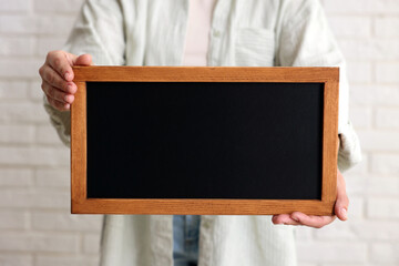 Woman holding blank small blackboard indoors, closeup