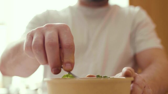 Closeup of man eating a fresh healthy salad from a zero waste container to go. Food delivery, healthy food concept.