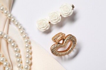Beautiful hair clips, pearl necklace and beige fabric on white background, flat lay
