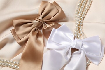 Beautiful hair bows and pearl necklace on beige fabric, above view