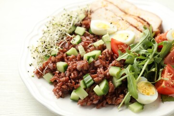 Delicious salad with brown rice on white wooden table, closeup