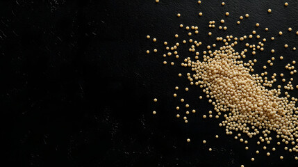 Obraz premium Amaranth grains, small, cream-colored, scattered across a dark, matte background, showcasing their fine texture and organic appearance.