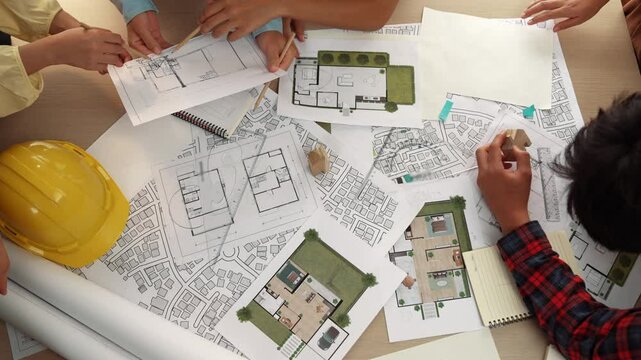 Architect and safety engineer discussion about building construction use blueprint on table with architectural document, measurement tool and wooden block scatter around at modern office. Delineation.