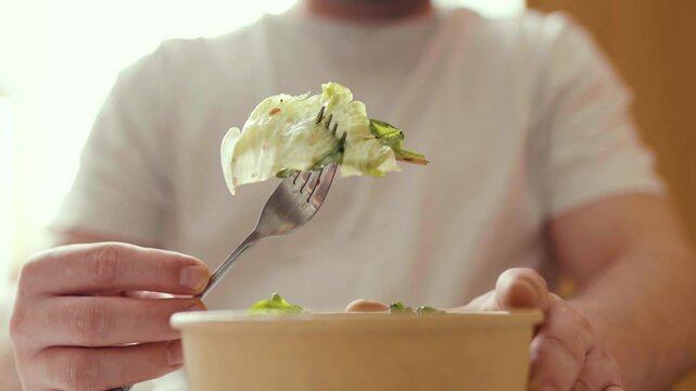 Closeup of man eating a fresh healthy salad from a zero waste container to go. Food delivery, healthy food concept.
