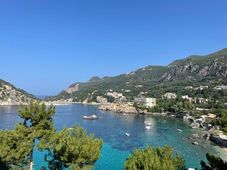 Obraz premium Elevated view of the stunning coastline in Paleokastritsa, Corfu, Greece, showcasing turquoise waters, lush green hills, and charming coastal buildings.