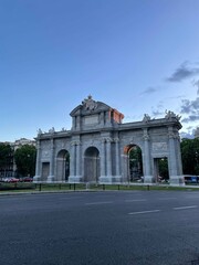 Obraz premium Stunning view of Puerta de Alcalá in Madrid at dusk with a serene blue sky. This neoclassical triumphal arch showcases intricate carvings and stands as an iconic landmark in Spain's vibrant capital.