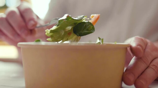 Closeup of man eating a fresh healthy salad from a zero waste container to go. Food delivery, healthy food concept.