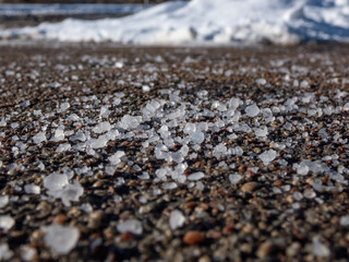 Close-up of white salt grains on icy sidewalk surface in the winter. Applying salt to keep roads clear and people safe in winter