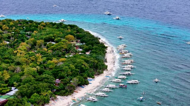 Balicasag, Philippines. Tropical circle form island in the ocean with coral reef around and many Philippine island hopping boats parked, sailing around. Drone aerial 4K video footage