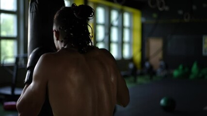 A skilled boxer is diligently practicing his punches against a heavy bag inside a dynamic, moody, well equipped gym