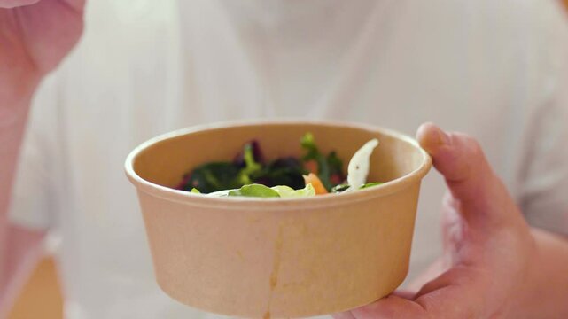 Closeup of man eating a fresh healthy salad from a zero waste container to go. Food delivery, healthy food concept.