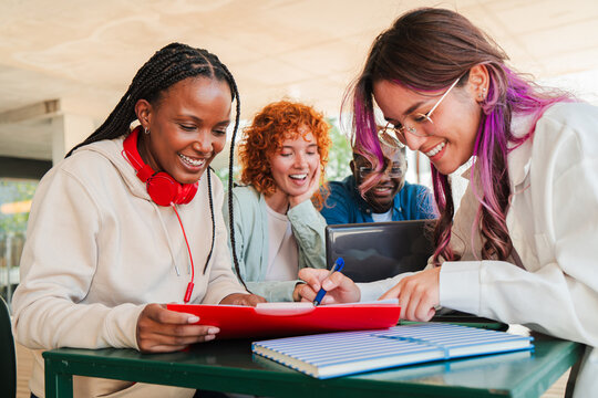 Excited diverse students engaged in collaborative learning while studying together and sharing ideas on homework assignments in a dynamic group setting during their university campus
