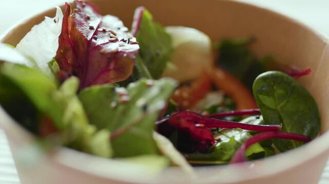 Closeup of man eating a fresh healthy salad from a zero waste container to go. Food delivery, healthy food concept.