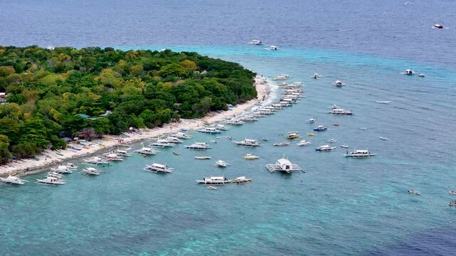 Balicasag, Philippines. Tropical circle form island in the ocean with coral reef around and many Philippine island hopping boats parked, sailing around. Drone aerial 4K video footage