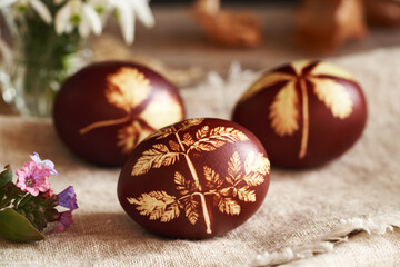Brown Easter egg dyed with onion skins with a pattern of fresh leaves, with spring flowers