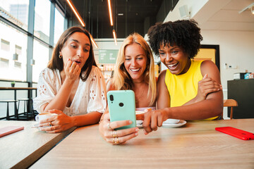 Three joyful women excitedly sharing a delightful moment while watching something amusing on their...