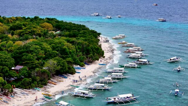 Balicasag, Philippines. Tropical circle form island in the ocean with coral reef around and many Philippine island hopping boats parked, sailing around. Drone aerial 4K video footage