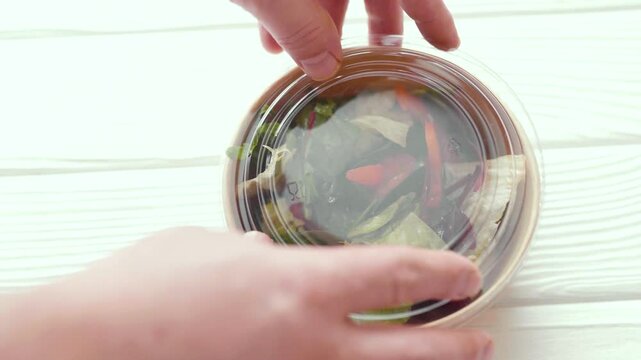 Closeup of man paking up a fresh healthy salad to a zero waste container to go. Food delivery, healthy food concept.