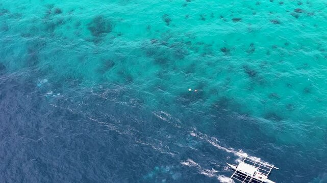 Close up of traditional Philippine island hopping boat sailing in turquoise color water over coral reef. Aerial 4K top view drone video footage