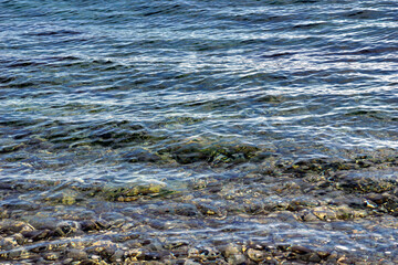 Horizontal waves on sea surface with light reflection above transparent clear seawater