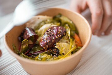 Closeup of man paking up a fresh healthy salad to a zero waste container to go. Food delivery, healthy food concept.