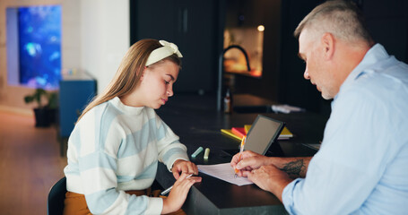 Obraz premium Girl, dad or writing with homework for assessment, tutoring or learning education at home. Father, teenager or helping daughter with assistance or marking paper for moderation, test or exam at house