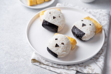 Rice ball onigiri with filling in the form of chicken with funny faces and with tamagoyaki in a plate