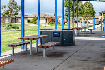A covered public seating area with sitting benches and a barbecue station offers a communal gathering space in a suburban park, providing public recreational amenities for the neighborhood.