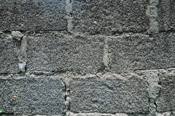 A rough-textured concrete brick wall with visible mortar lines, captured in black and white, emphasizing texture and contrast in an urban setting.