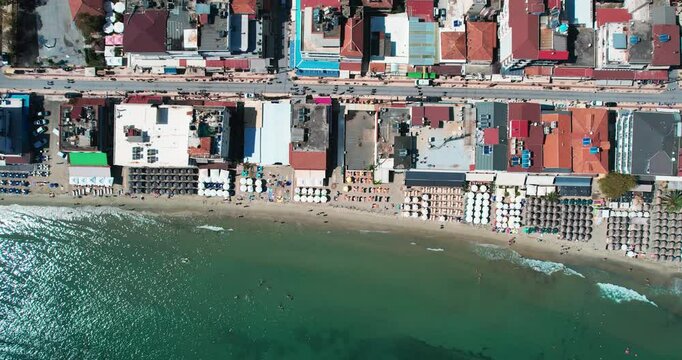 Aerial view of Paralia, Greece, reveals vibrant beachfront resorts and glittering waters. The scene captures colorful umbrellas, lively seaside activities, and a distinct summer vacation atmosphere