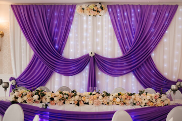 A luxurious wedding hall decorated with purple drapery and floral arrangements.