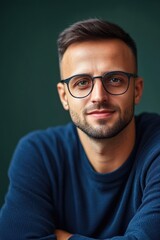 Young caucasian male with glasses in blue sweater against dark green background