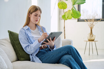Obraz premium Young woman using digital tablet sitting on sofa at home