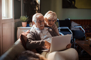 Elderly couple embracing while using laptop at home
