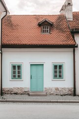Nestled in a picturesque village, this delightful white cottage features a charming mint green door and windows, beautifully set against a cloudy afternoon sky