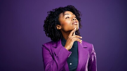 A thoughtful woman in a purple blazer poses against a purple backdrop. The video captures her from a medium angle, emphasizing her contemplative expression.