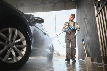 A car wash worker is using high pressure water gun for car washing