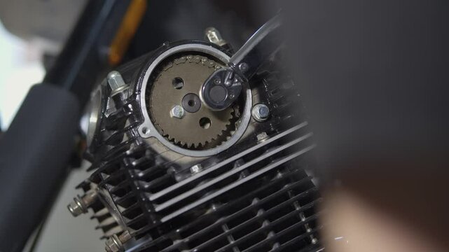 A mechanic repairs a motorcycle engine using a torque wrench to check the tightness of the bolts on the timing gear