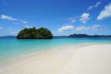 Fototapeta premium a beautiful tropical beach with clear blue water, white sand, and a small island in the background. The sky is partly cloudy with a few white clouds.