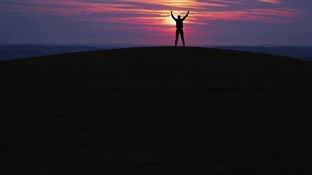 Silhouette of a person with raised arms on a hilltop at sunset, captured from a low-angle, evoking triumph and freedom. Ideal for inspirational video content. Live desktop wallpaper.