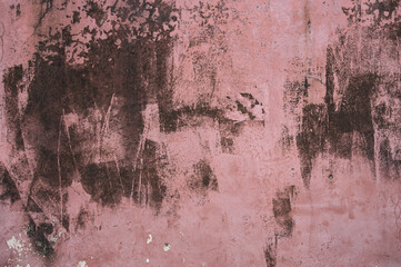 A weathered pink wall with dark stains and peeling paint, creating an abstract and textured urban aesthetic. The rough patterns evoke decay and artistic grunge.